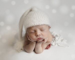 Baby wearing knitted hat sleeps on white blanket